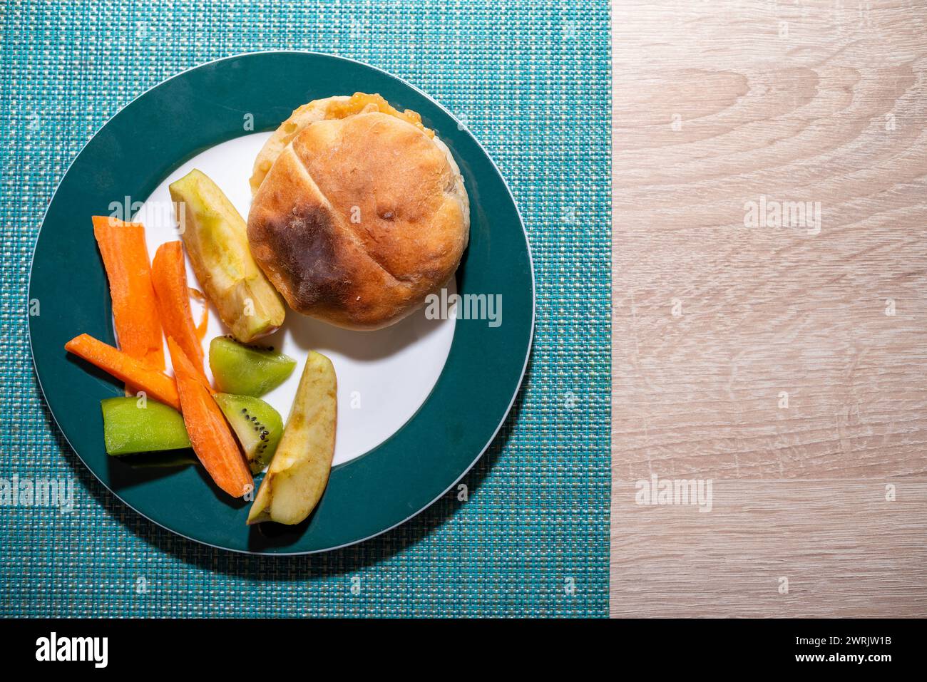 A plate with a bun, carrots, and pickles on a table Stock Photo