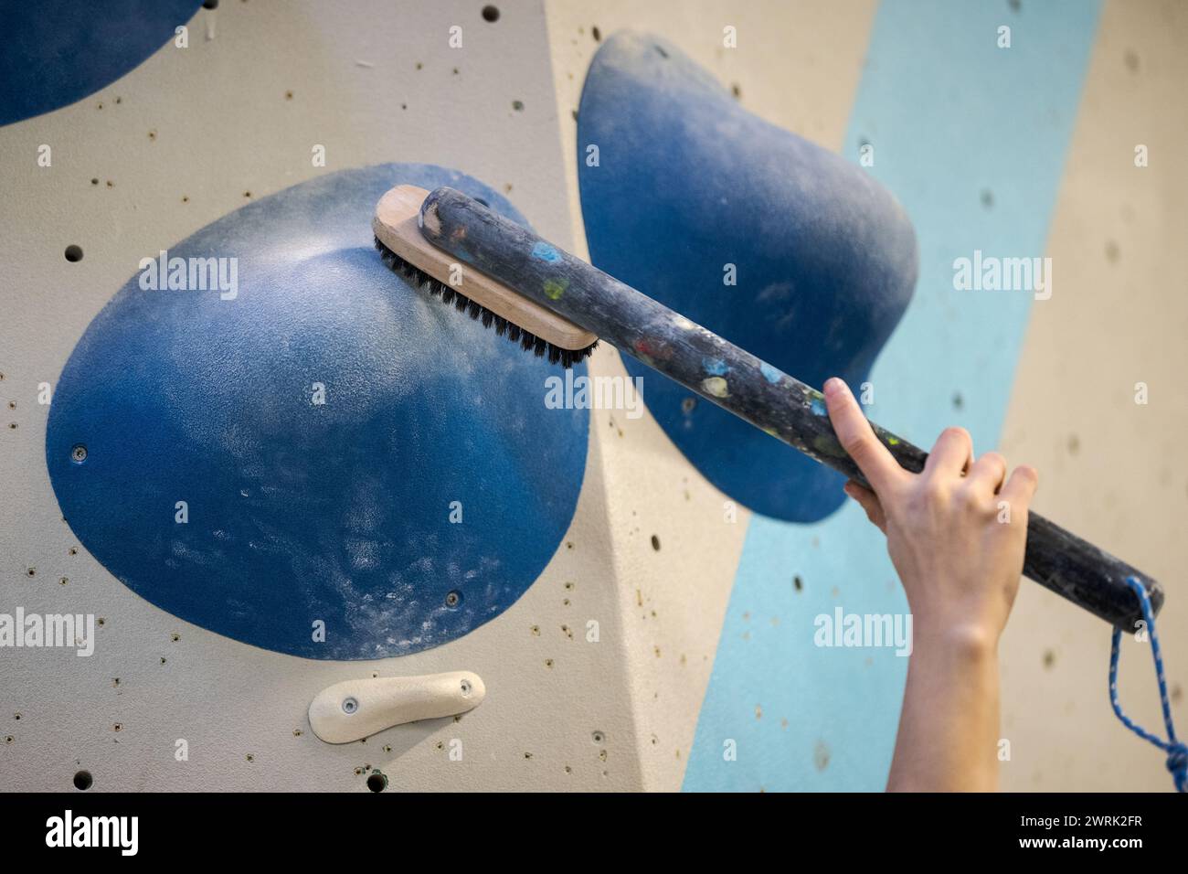 Hand holding big brush on long stick in bouldering climbing gym brushing off chalk of a large hold for the hands Stock Photo