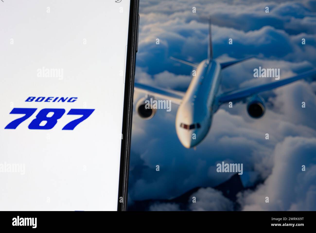 Boeing 787 logo is sharp in the foreground, while flying airplane is blurred in the background. Stock Photo