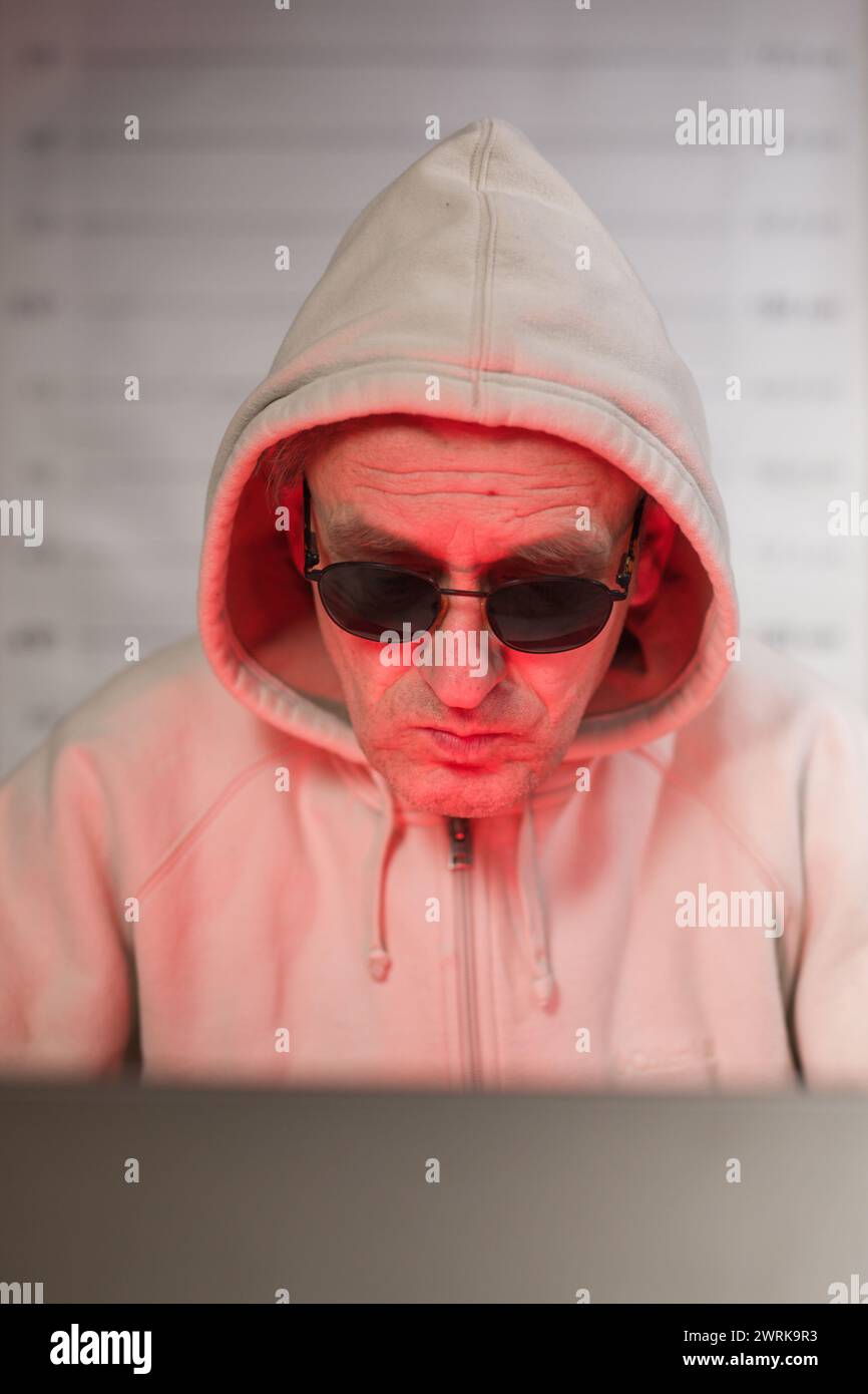 Older criminal man using computer for remote money robbery Stock Photo