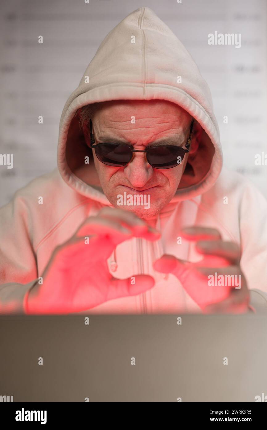 Older criminal man using computer for remote money robbery Stock Photo