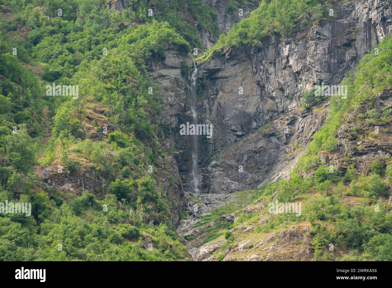 Norwegian fjord mountain nature view with a waterfall that has washed a cave in the mountain and green trees growing at the foot of the mountain Stock Photo