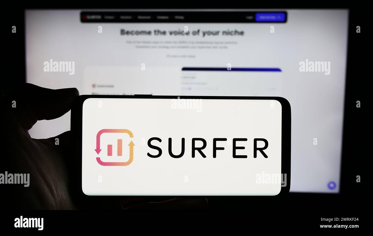 Person holding cellphone with logo of Polish AI company Surfer sp. z o.o. (SurferSEO) in front of business webpage. Focus on phone display. Stock Photo