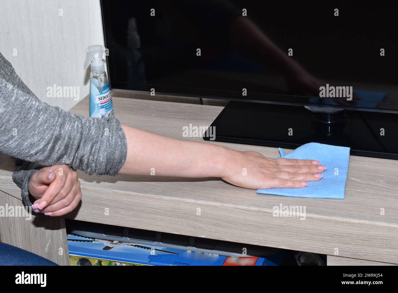 The hostess is cleaning, she wipes the dust from the surface of the nightstand on which the TV stands with a napkin. Stock Photo