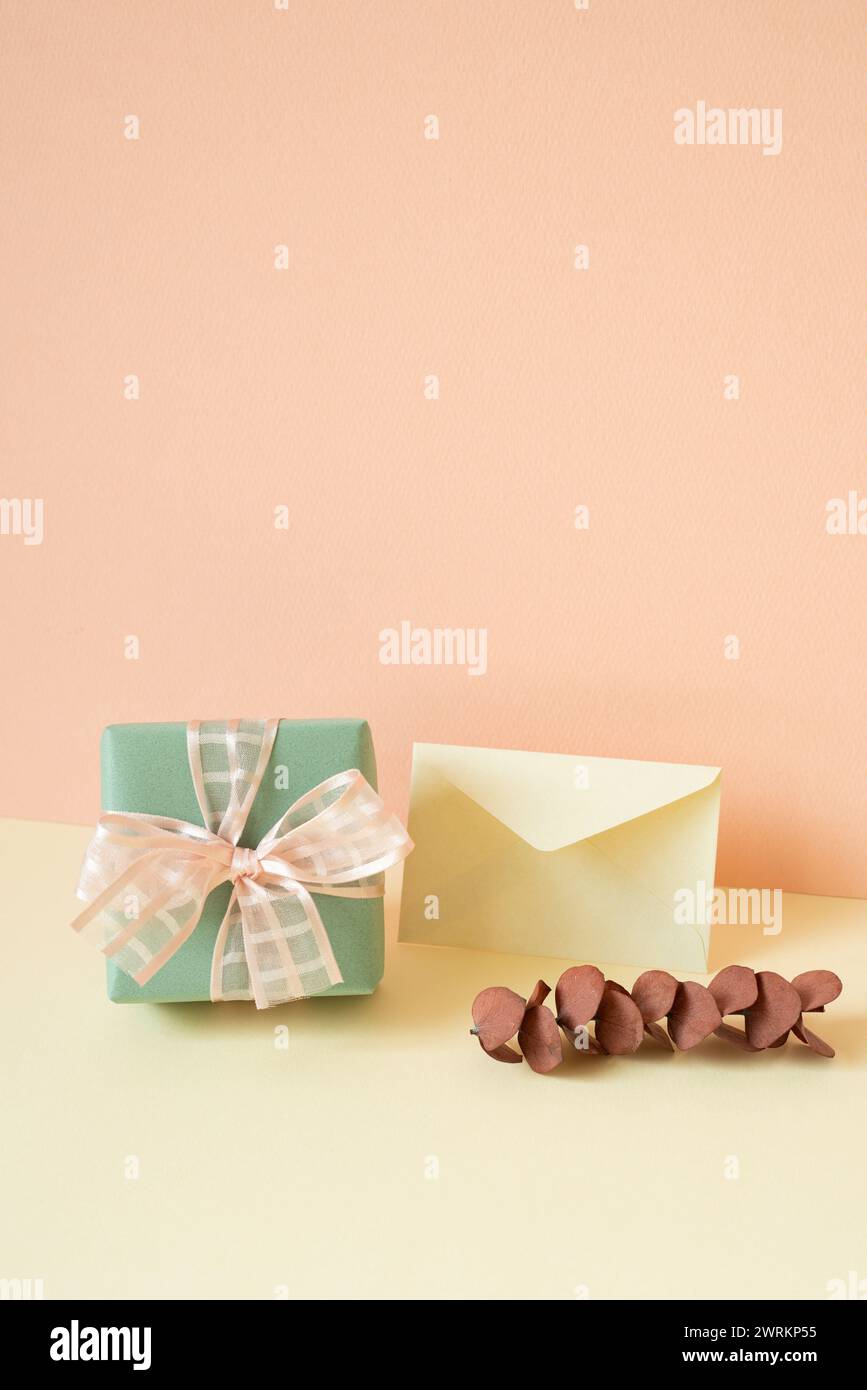 Green gift box, envelope, eucalyptus leaf on ivory table. pink wall background Stock Photo