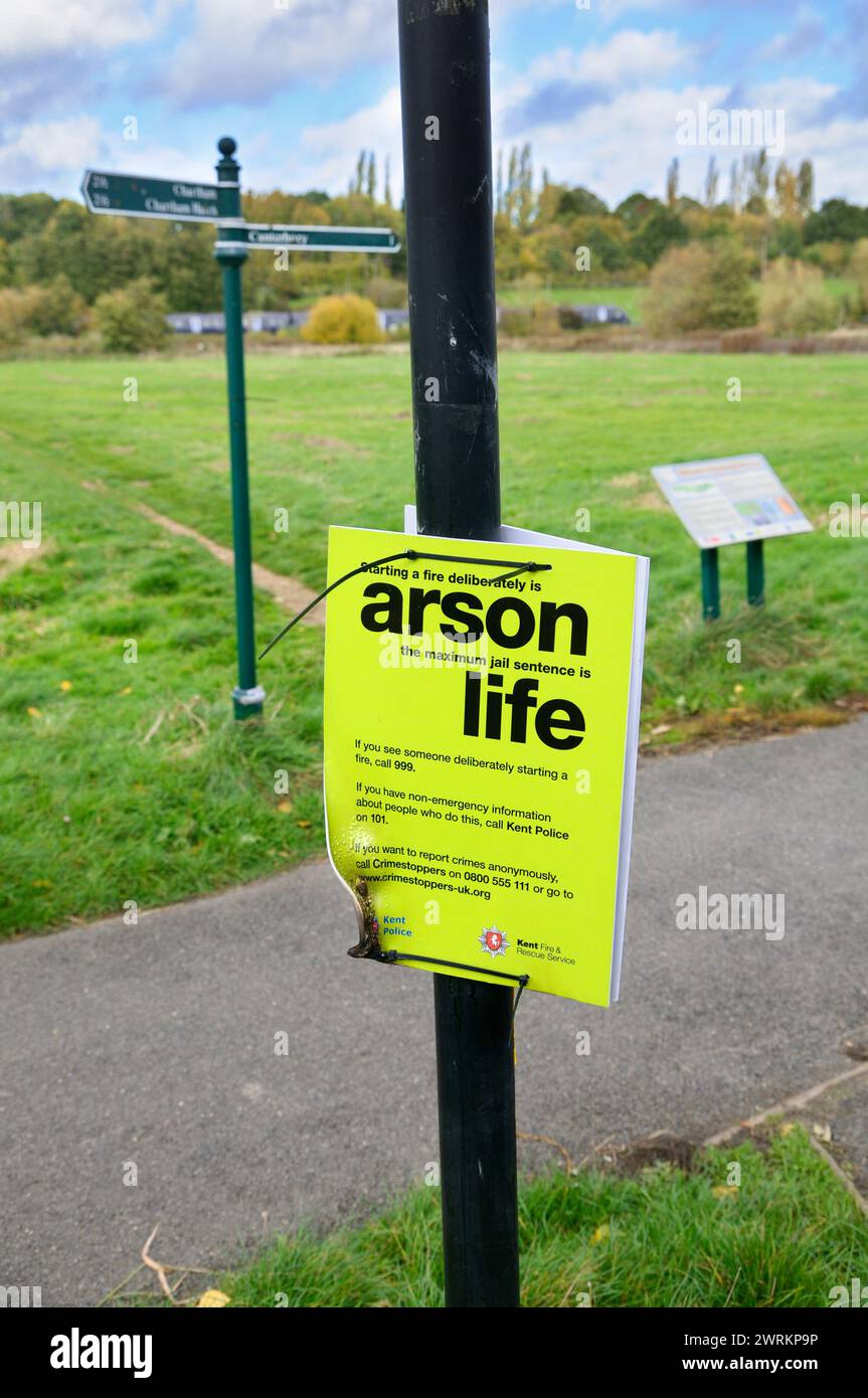 Police sign on a park lamp post warning public of serious penalties for arson.  The sign has been vandalised with a flame and is melted and warped. UK Stock Photo