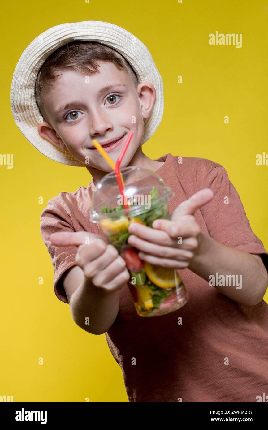 Cute boy with Mojito cocktail from plastic cup over yellow background ...