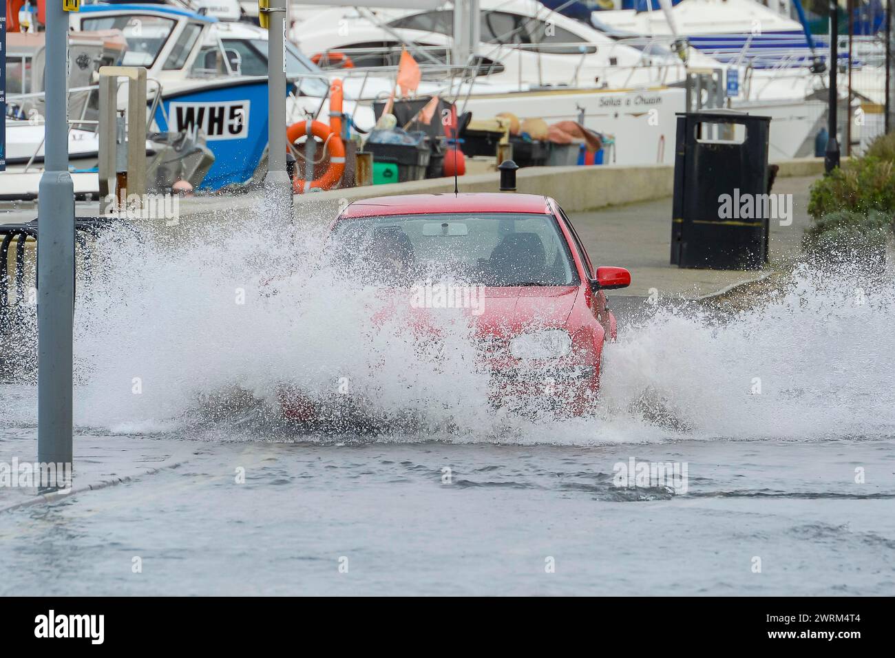 Weymouth, Dorset, UK.  13th March 2024. UK Weather:  A car drives through floodwater from a high spring tide on Commercial Road next to the harbour at Weymouth in Dorset on a warm overcast morning.  Picture Credit: Graham Hunt/Alamy Live News Stock Photo