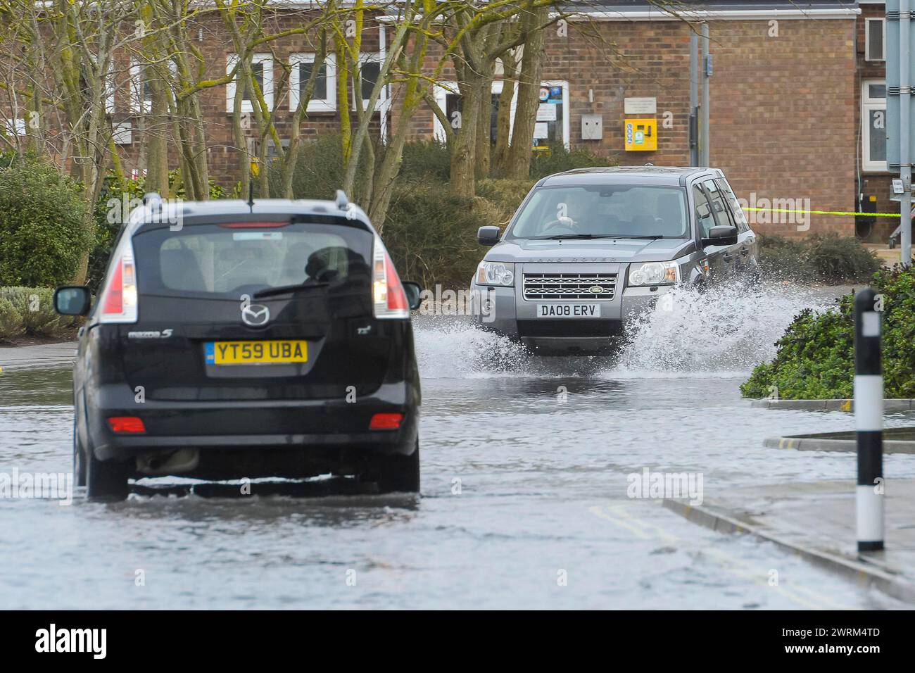 Weymouth, Dorset, UK.  13th March 2024. UK Weather:  Cars drive through floodwater from a high spring tide on Commercial Road next to the harbour at Weymouth in Dorset on a warm overcast morning.  Picture Credit: Graham Hunt/Alamy Live News Stock Photo