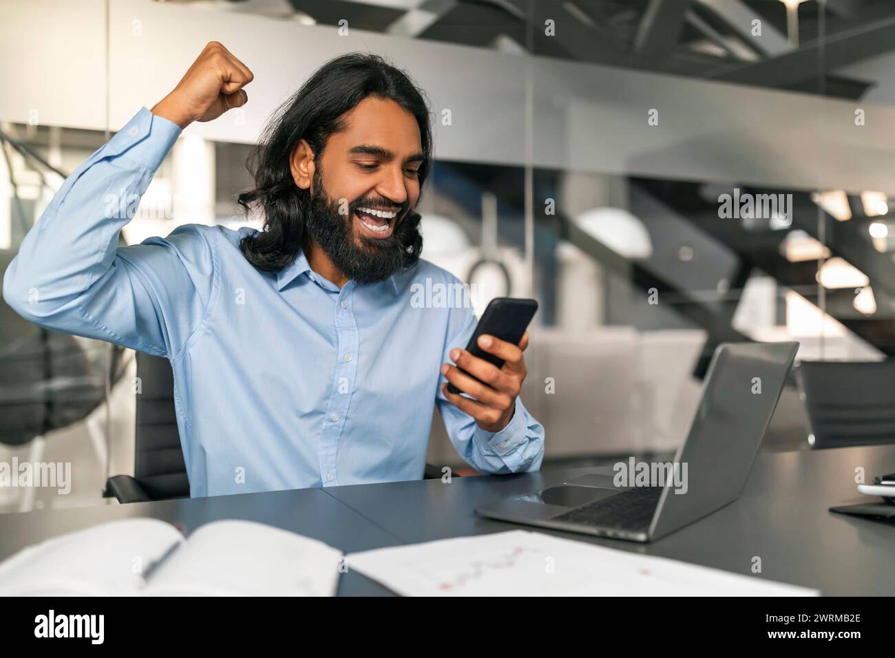 Excited indian guy manager looking at smartphone screen, gesturing Stock Photo