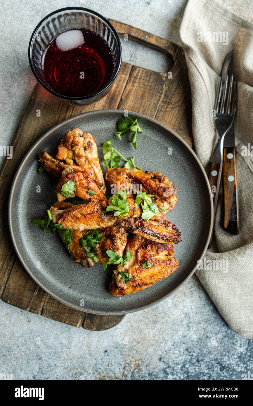 Top view succulent roasted chicken wings in a spicy sauce garnished with fresh coriander leaves, served alongside a refreshing glass of cherry cocktai Stock Photo