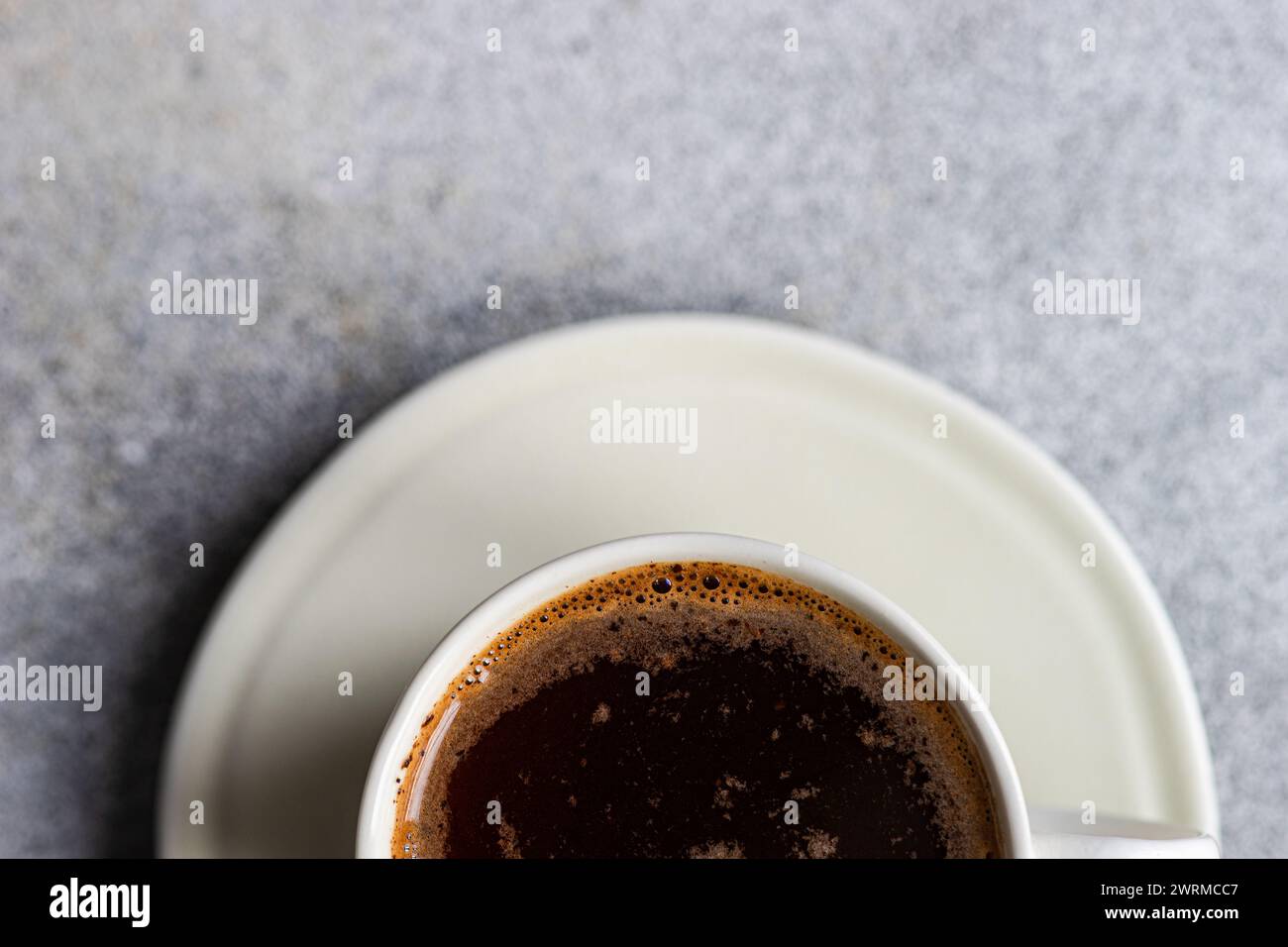 A top view of a freshly brewed hot coffee in a white cup placed on a saucer, with a foamy surface, perfect for a morning energy boost. Stock Photo