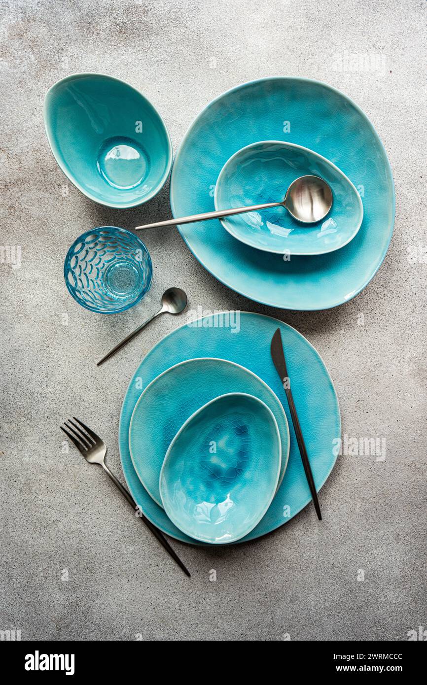 Top view of a stylish turquoise ceramic table setting with matching cutlery on a textured surface. Stock Photo