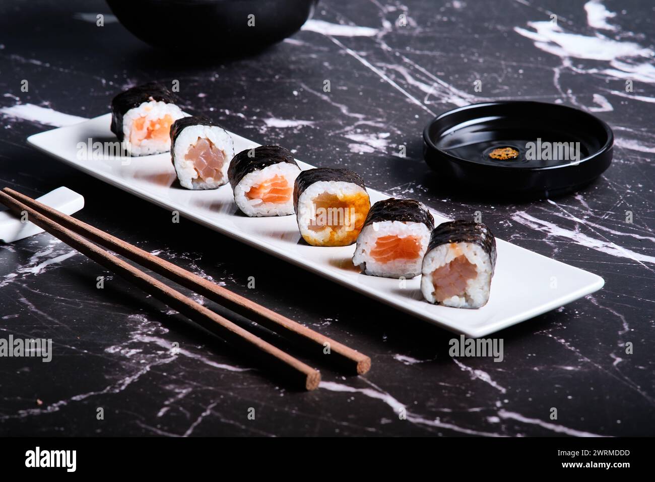 Assorted sushi rolls served on a white plate with soy sauce and chopsticks on a dark marble background. Stock Photo