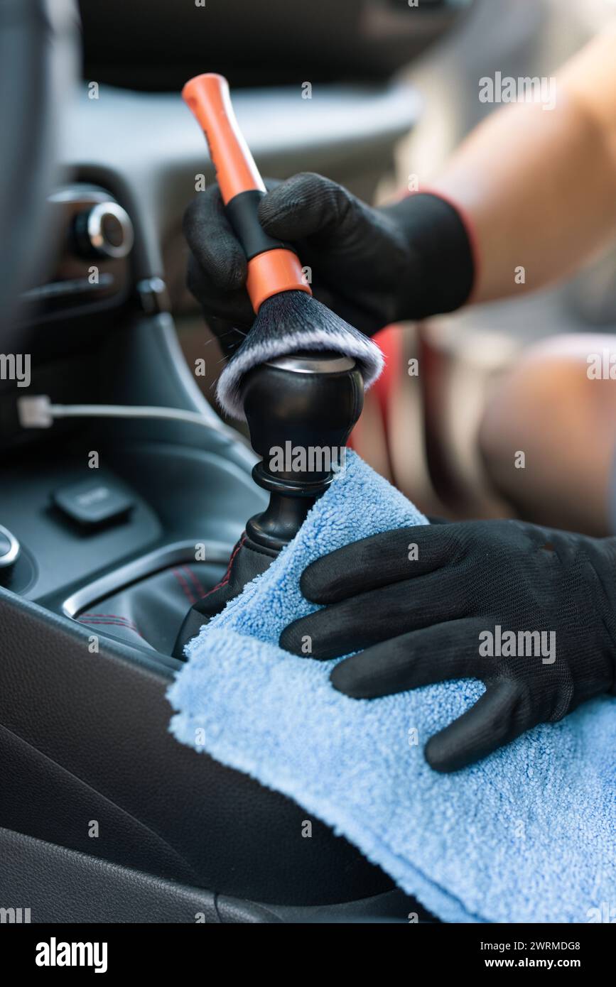 Close-up of hands dusting a car gear shift with a detailing brush and a microfiber cloth Stock Photo