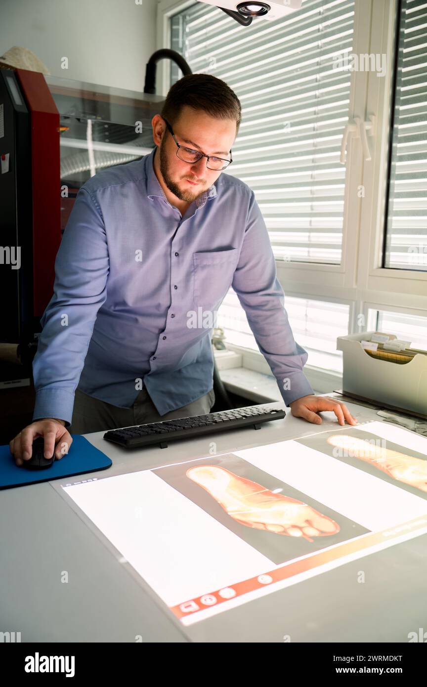 A male shoemaker in Austria attentively examines footwear designs on a digital screen, preparing for the crafting process. Stock Photo