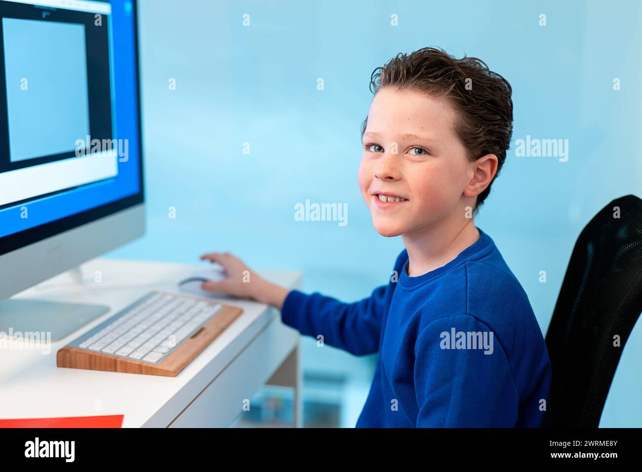 A smiling boy enjoys his time on the computer, possibly participating in a virtual class or exploring educational software Stock Photo