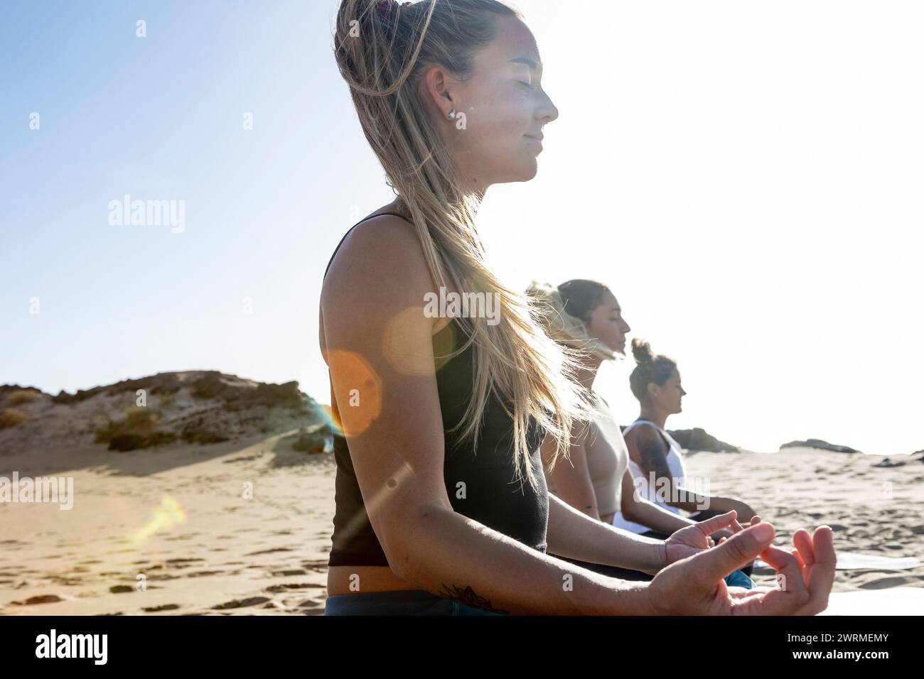 women practice yoga in the peaceful evening ambiance of a beach setting, with gentle waves and the sunset providing a serene backdrop. Stock Photo