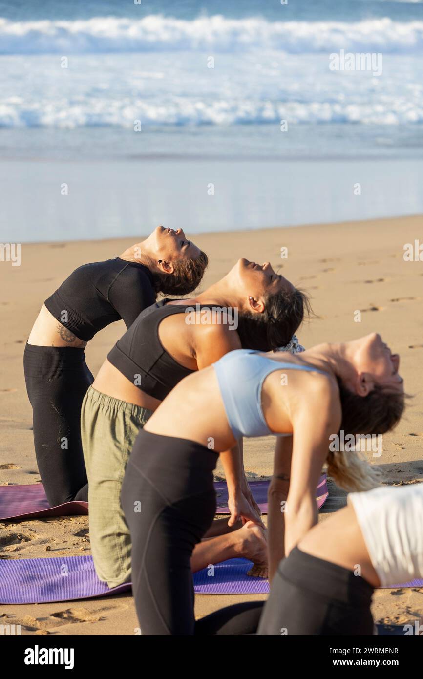 Practitioners perform yoga backbends on the beach during a peaceful session, embodying wellness and harmony with the natural surroundings. Stock Photo