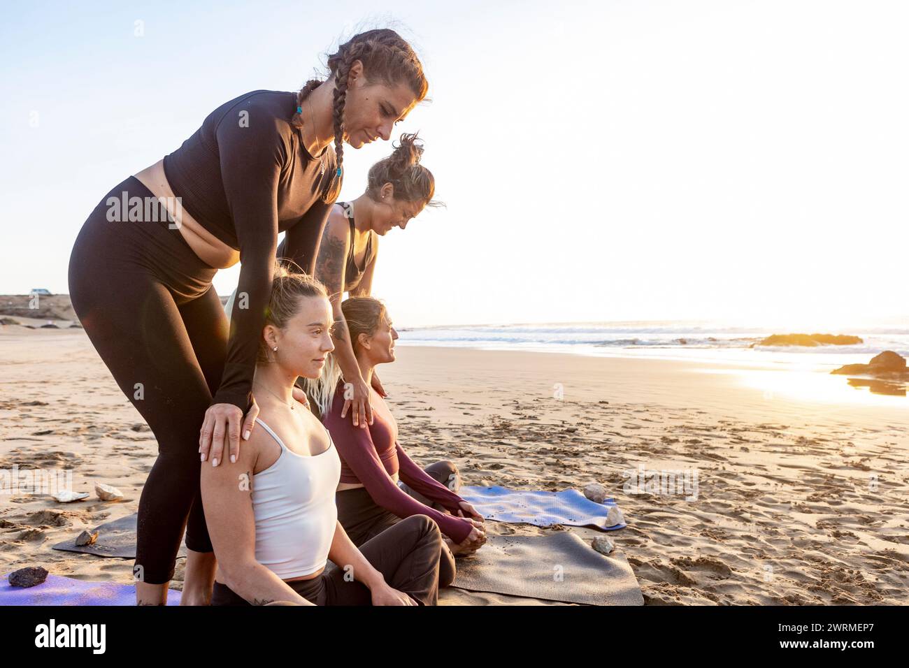 A serene yoga class unfolds on a sandy beach at sunset, with participants engaging in various poses under the guidance of an instructor. Stock Photo