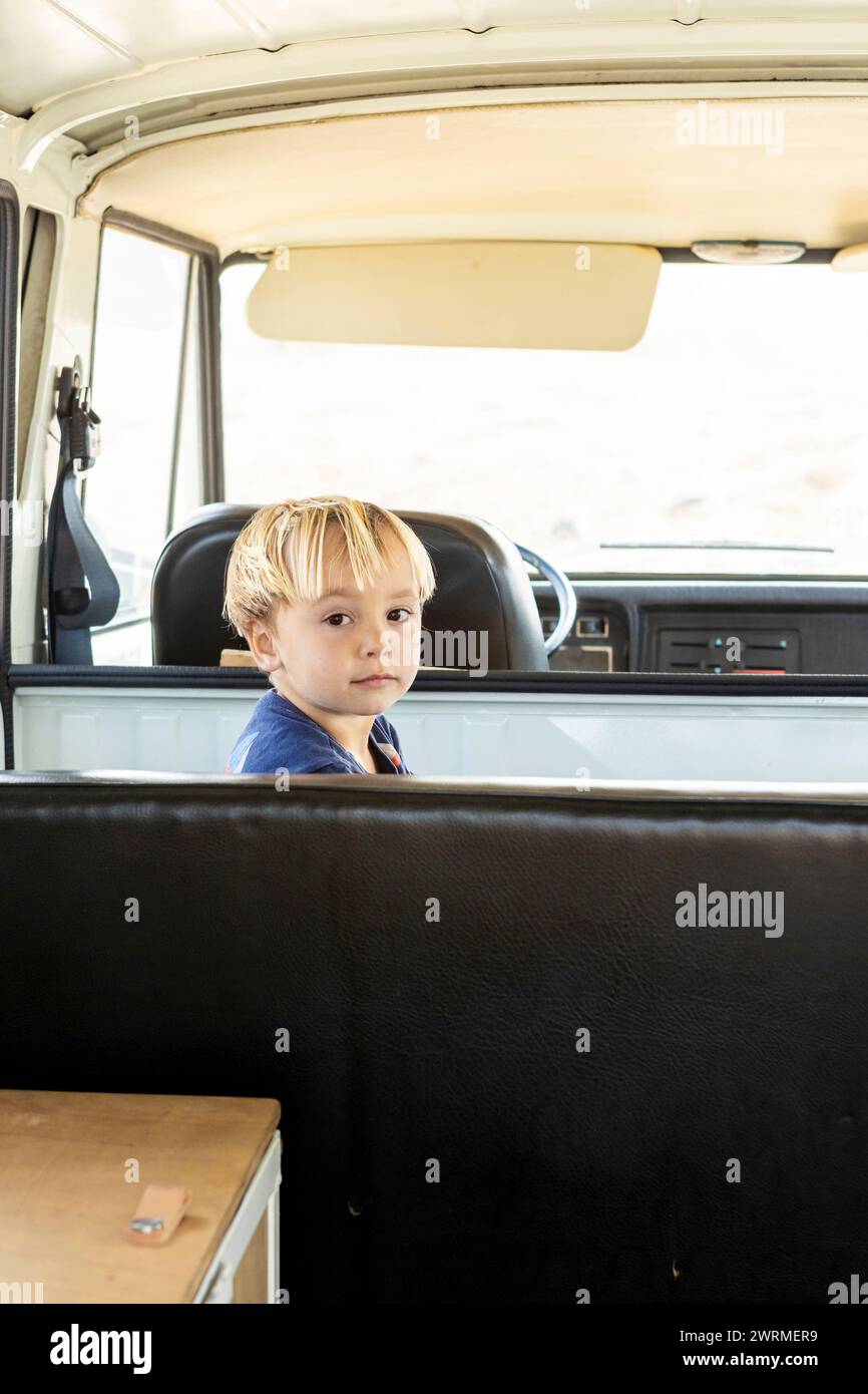 Candid portrait of a young boy seated in a vintage van, symbolizing family adventures and the joy of simple travel. Stock Photo