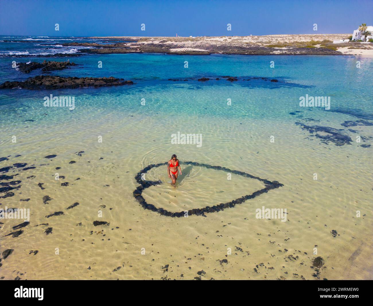 Aerial view of a woman standing inside a heart shape drawn in the sandy ...