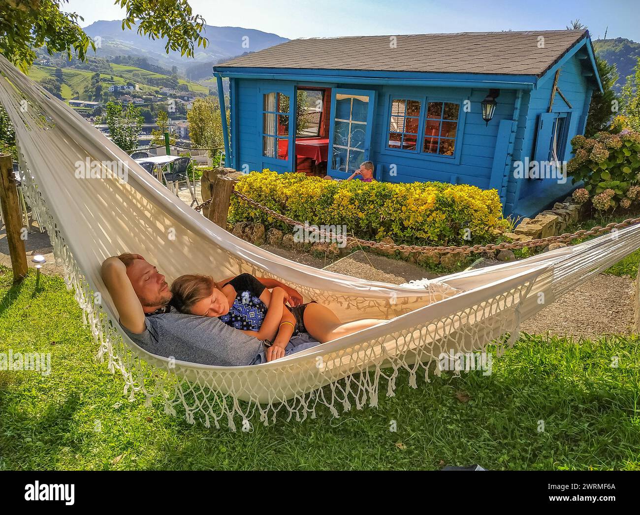Couple sleeping in hammock on backyard. Quiet hour in french village. Man and woman having rest on rural landscape background. Peaceful moment. Stock Photo