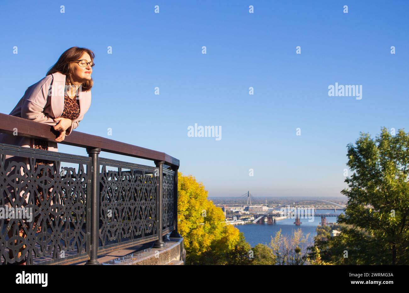 Woman in leopard dress and coat on Kyiv landscape background. Woman in glasses smiling in sunlight. Big city lifestyle. Beautiful woman in Ukraine. Stock Photo