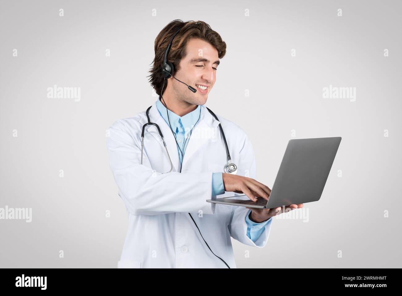 Smiling man doctor with headset using laptop for telehealth services Stock Photo
