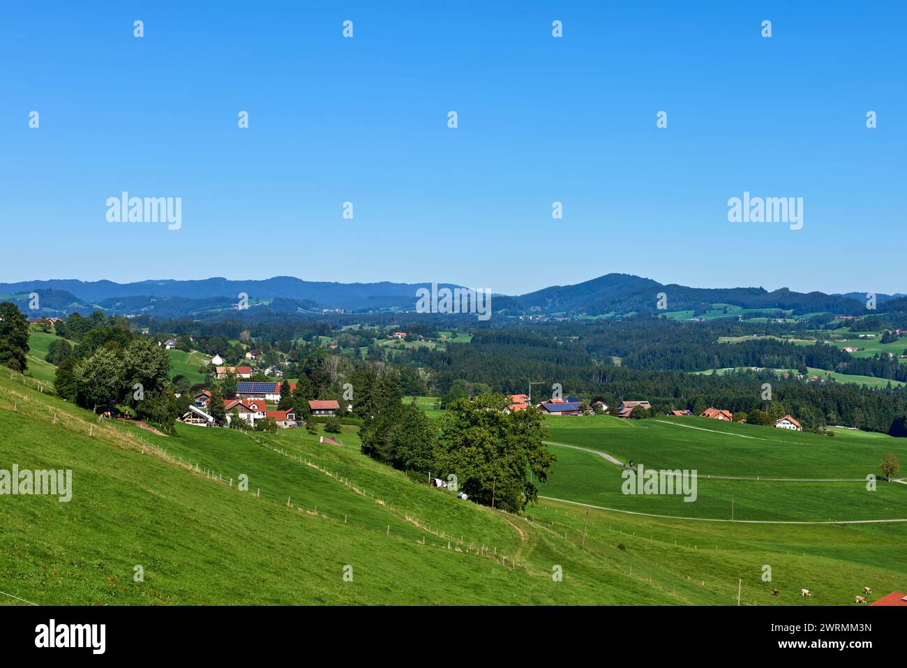 Alpine Foothills Charm: Rural Mountainside Living with Farmer's Homesteads. Mountain Countryside: Farmer's Dwellings, Pastures, and the Sky Above Stock Photo