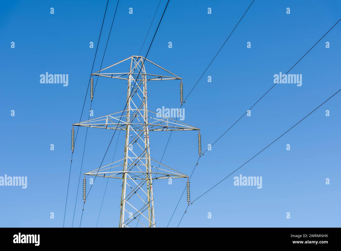 Overhead 132kv electricity transmission cables and transmission tower against a blue sky. Stock Photo