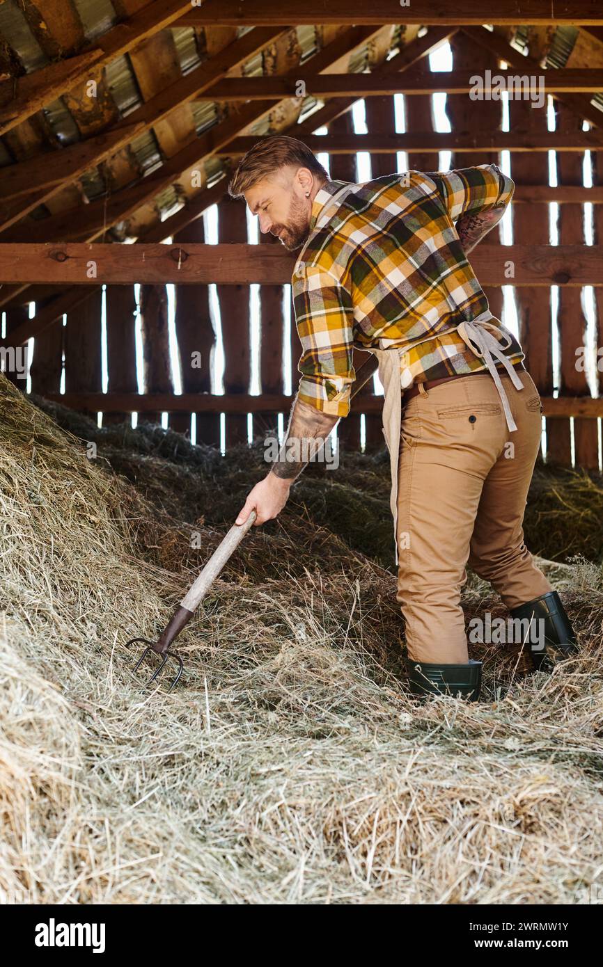cheerful good looking man with tattoos using pitchfork while working