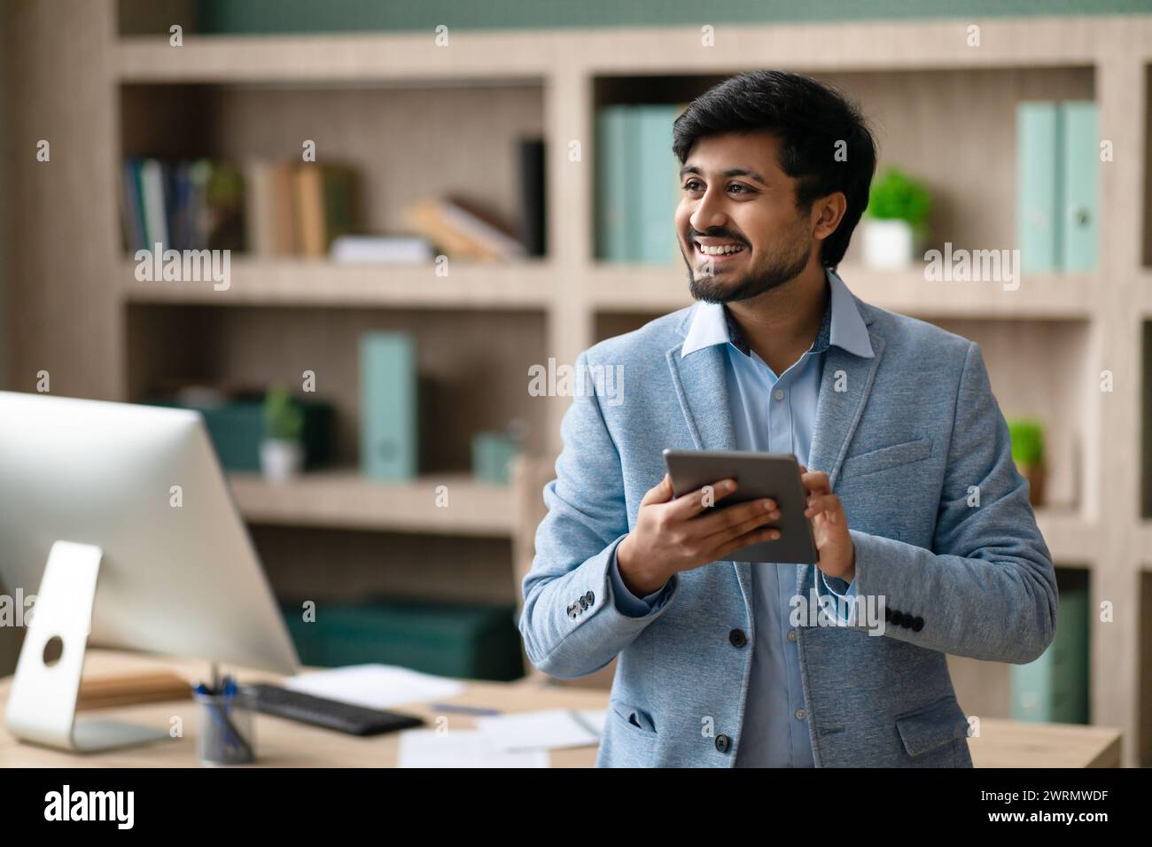Happy Indian programmer man using tablet standing in modern office Stock Photo