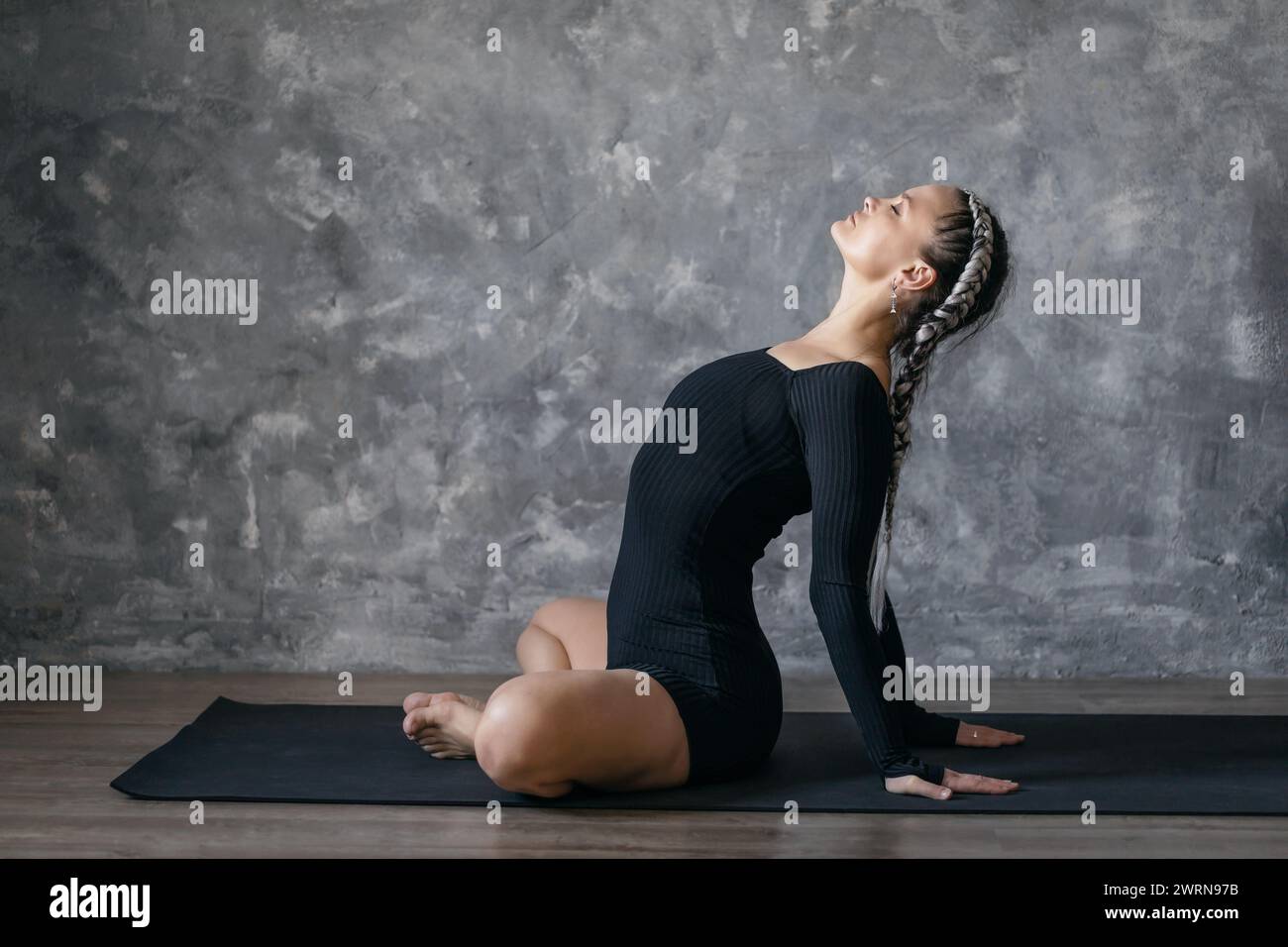 An attractive woman leading a healthy lifestyle performs calming backbends with her hands behind her back while sitting on a mat, training in sports b Stock Photo