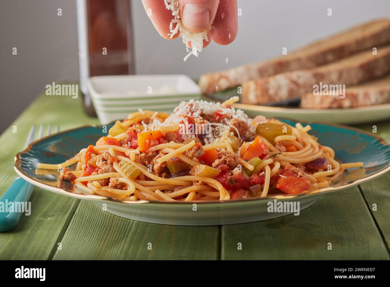 Turkey mince bolognese with cheese being sprinkled over it and some bread in the background. Stock Photo