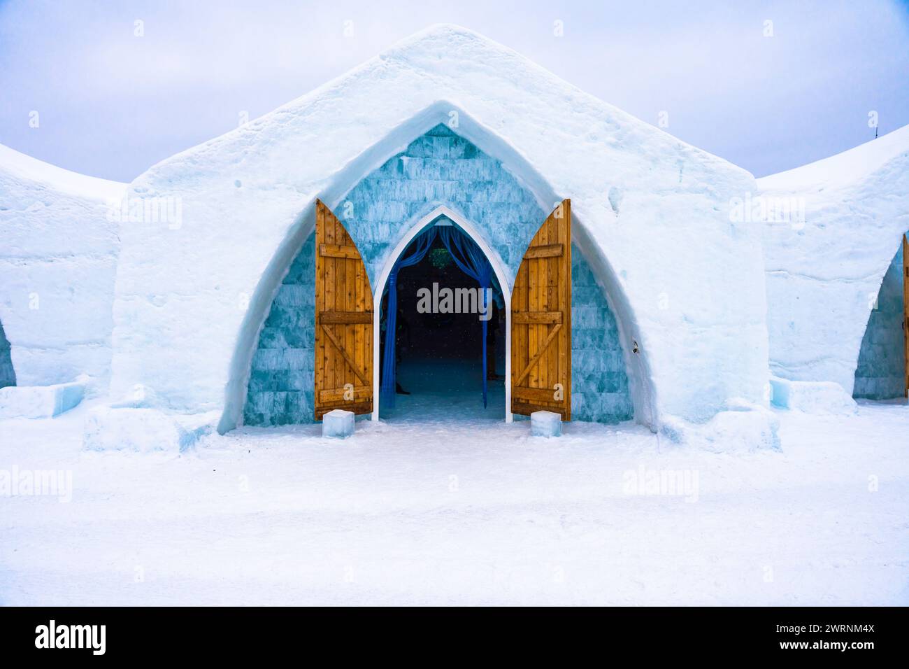 Modernized Igloo with wooden door and ice blue entrance to opened building made entirely of ice during blizzard Stock Photo