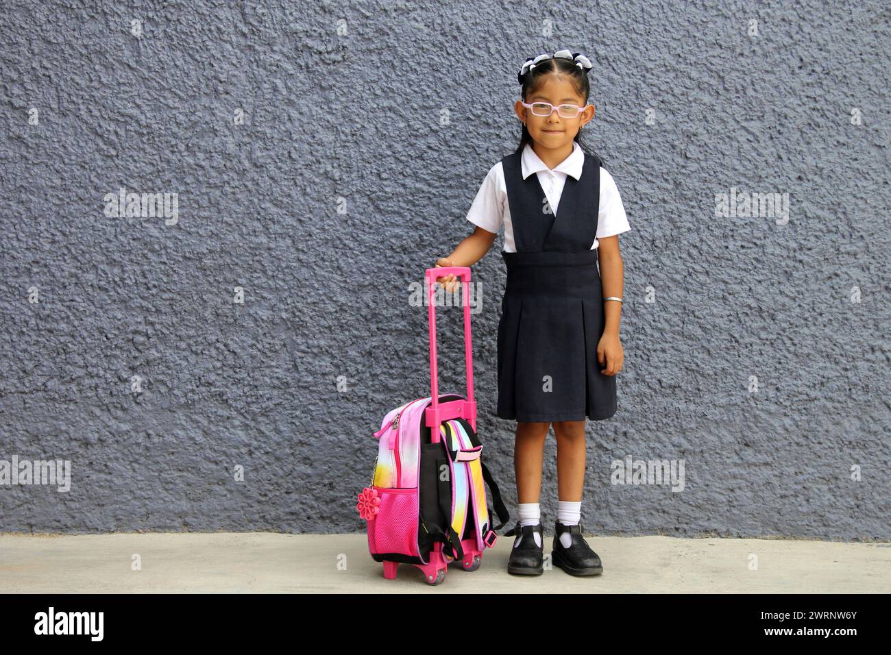 4 year old Latina brunette girl with eyeglasses, uniform and backpack walks to school this back to school Stock Photo