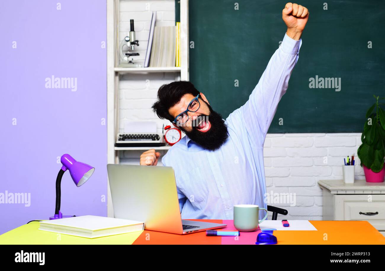 Happy male teacher or student in classroom. Bearded businessman professional coach, teacher or university professor sitting at desk in office Stock Photo