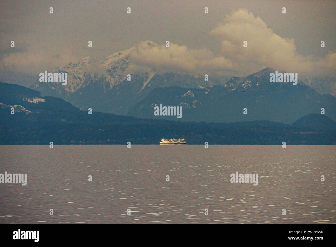 Photo of a distant ferry with clouds snowcapped mountains in the background off the coast of Vancouver Island, near Nanaimo B.C. Stock Photo