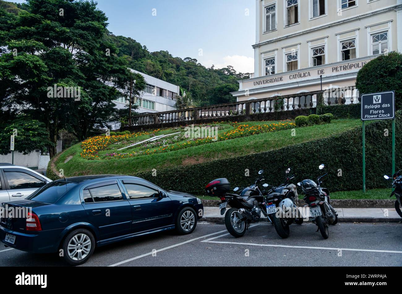 Vehicles parked in the parking spaces in front of the Flower Clock at Catholic University of Petropolis in Centro district under summer afternoon. Stock Photo