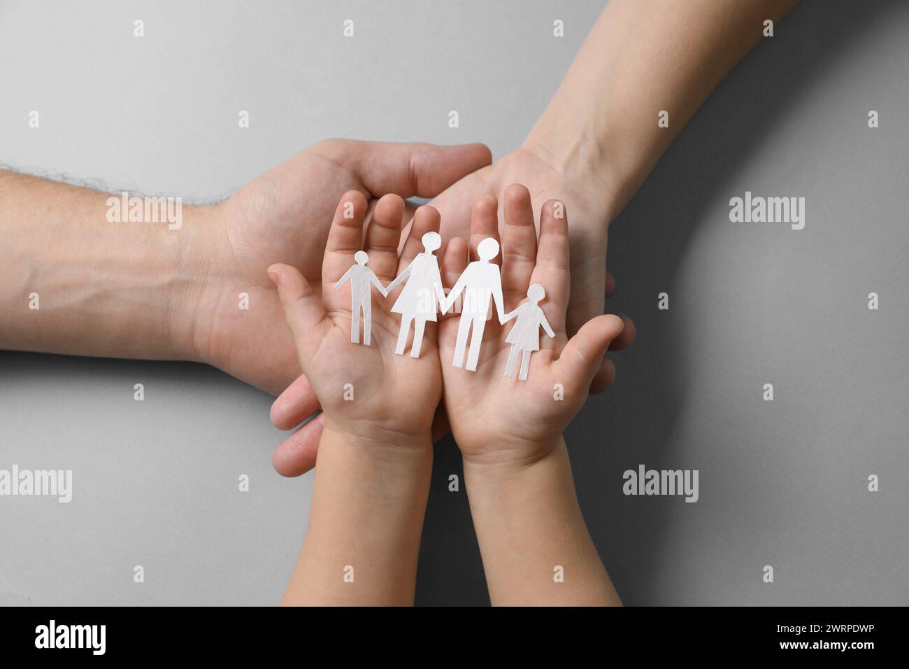 Parents and child holding paper family figures on gray background, top ...