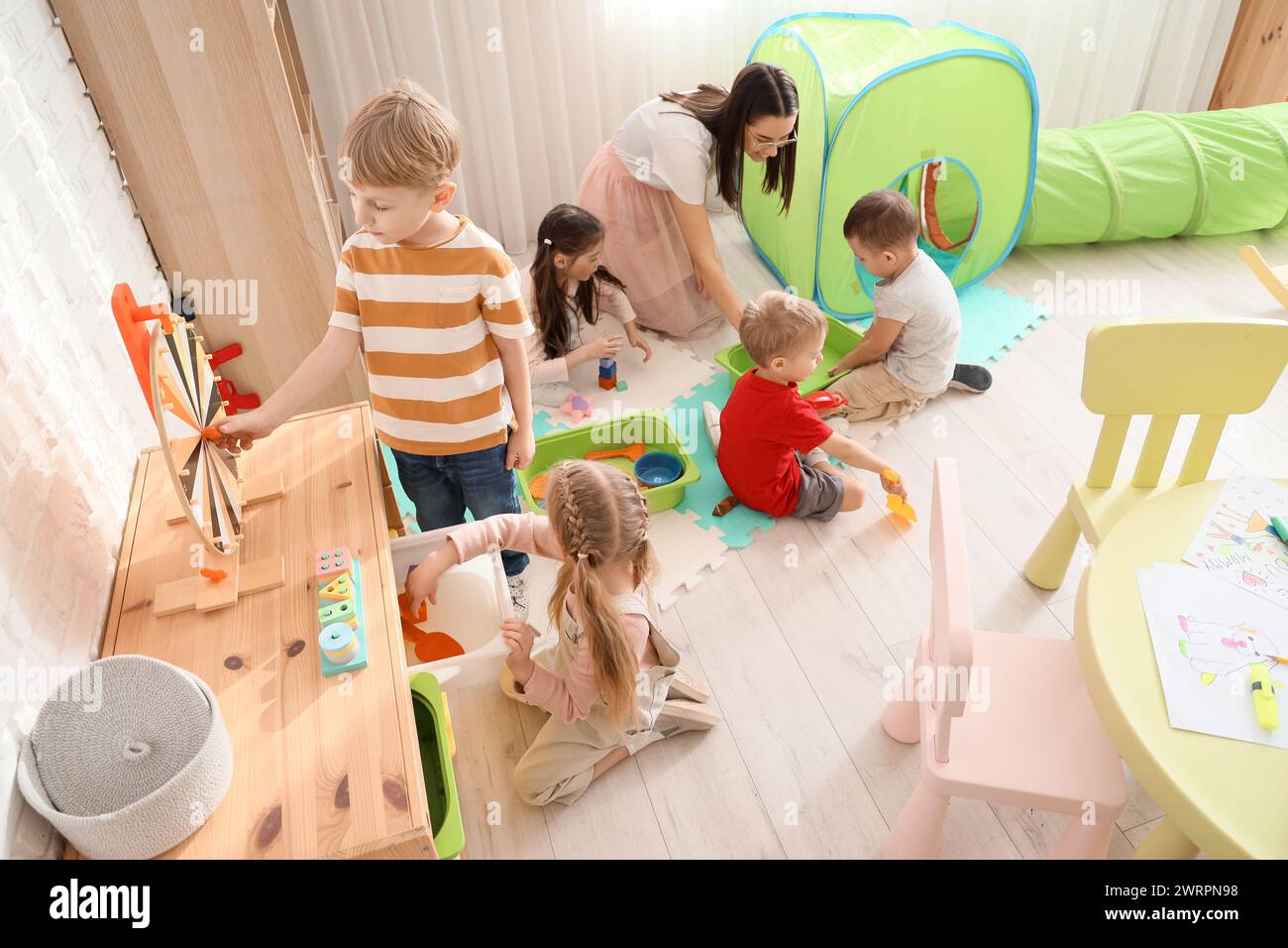 Little children and nursery teacher playing with toys in kindergarten Stock Photo