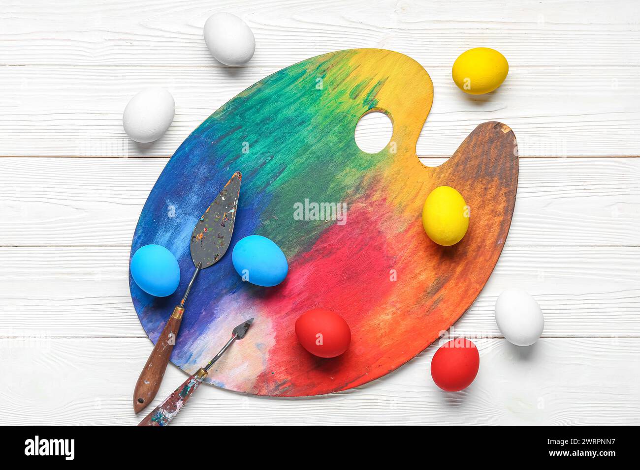 Paint palette and Easter eggs on wooden white background. Easter concept. Stock Photo