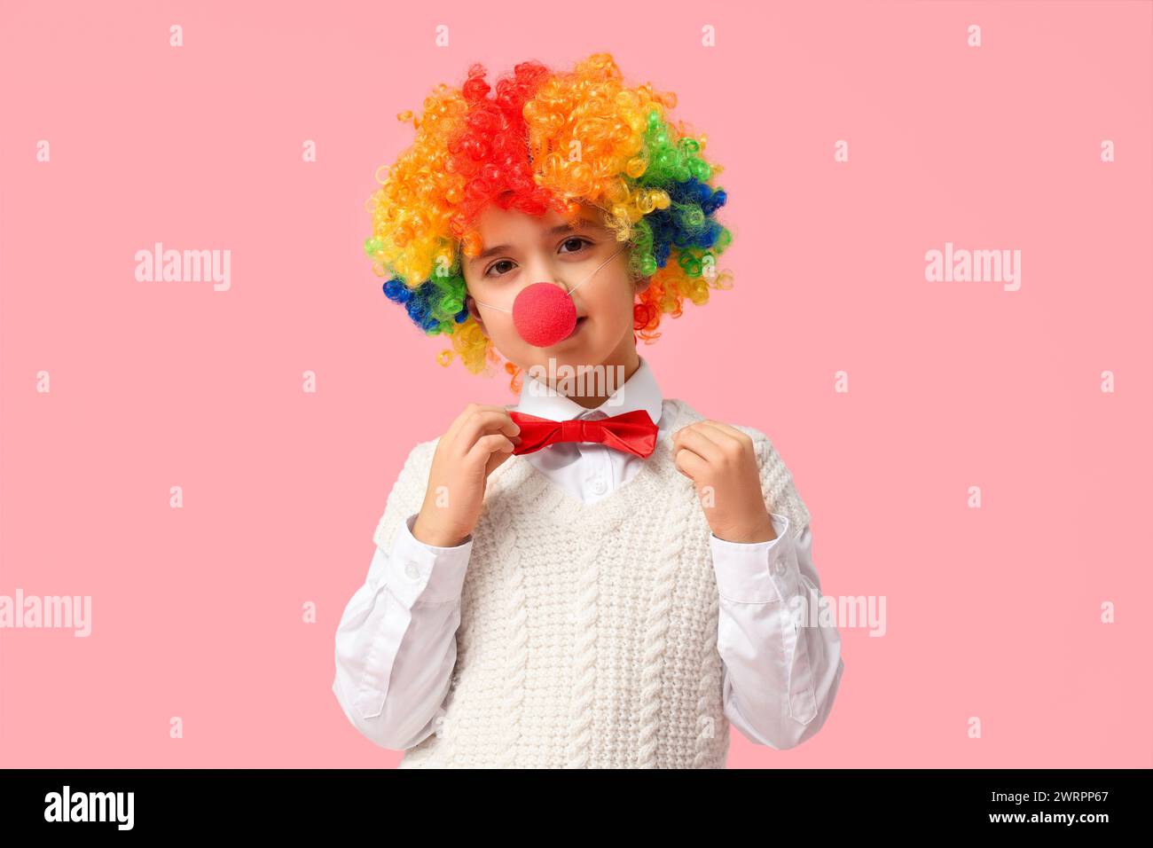 Funny little boy in clown wig and nose on pink background. April Fools