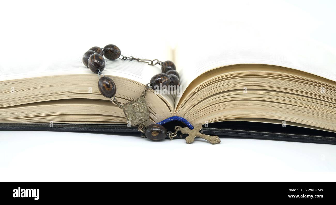 Open book with a rosary carefully laid on top of the pages placed against a white background, emphasizing spirituality and the intrinsic link between Stock Photo