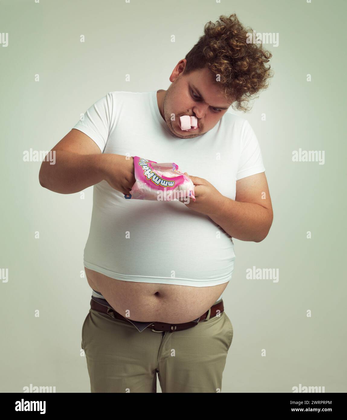 Obesity, weight gain and comic for man in studio with marshmallow for unhealthy eating, sugar and candy. Overweight person with hand in sweet packet Stock Photo