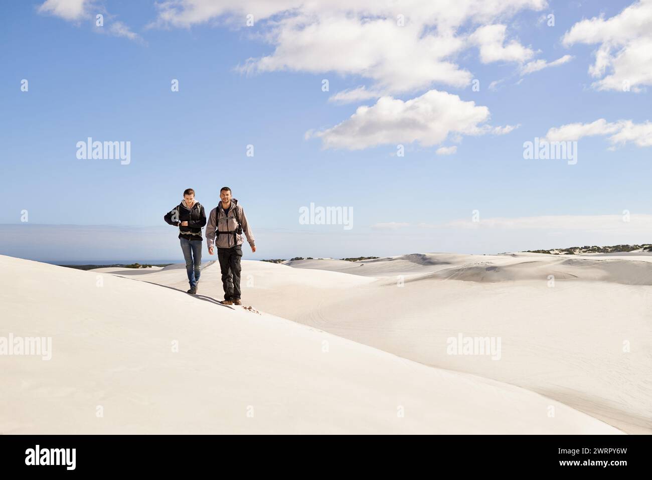 Couple, hiking and sand outdoor or desert with dune, sky and clouds for walking, climbing and move for recreation. Man, woman and young for adventure Stock Photo