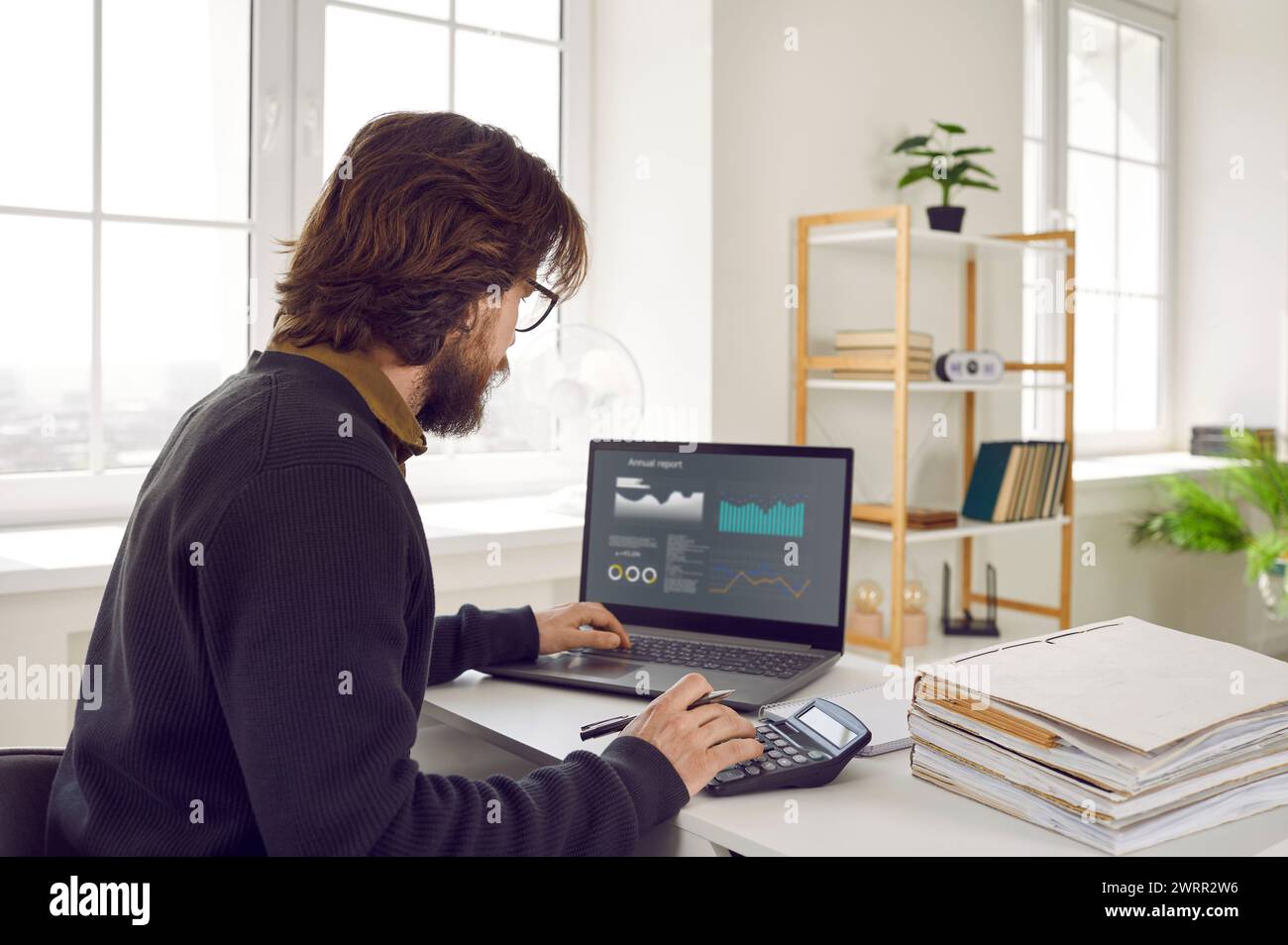 Man sitting at office desk, using laptop computer and working with financial data Stock Photo