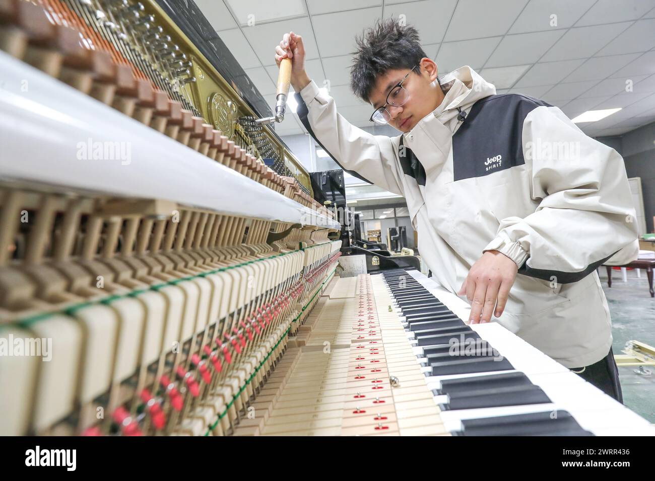 HUZHOU, CHINA - MARCH 14, 2024 - A technician is adjusting the timbre of a piano at a workshop of a piano company in Huzhou, East China's Zhejiang pro Stock Photo