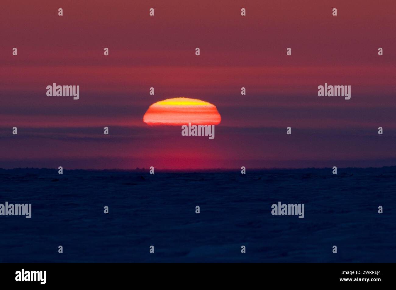 late winter sunsetting just over the horizon beyond the pack ice over the Beaufort sea and off shore from the arctic village of Kaktovik Alaska Stock Photo